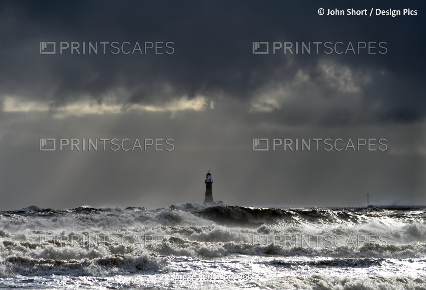 Roker Lighthouse and stormy waters splashing in the foreground with sunlight ...