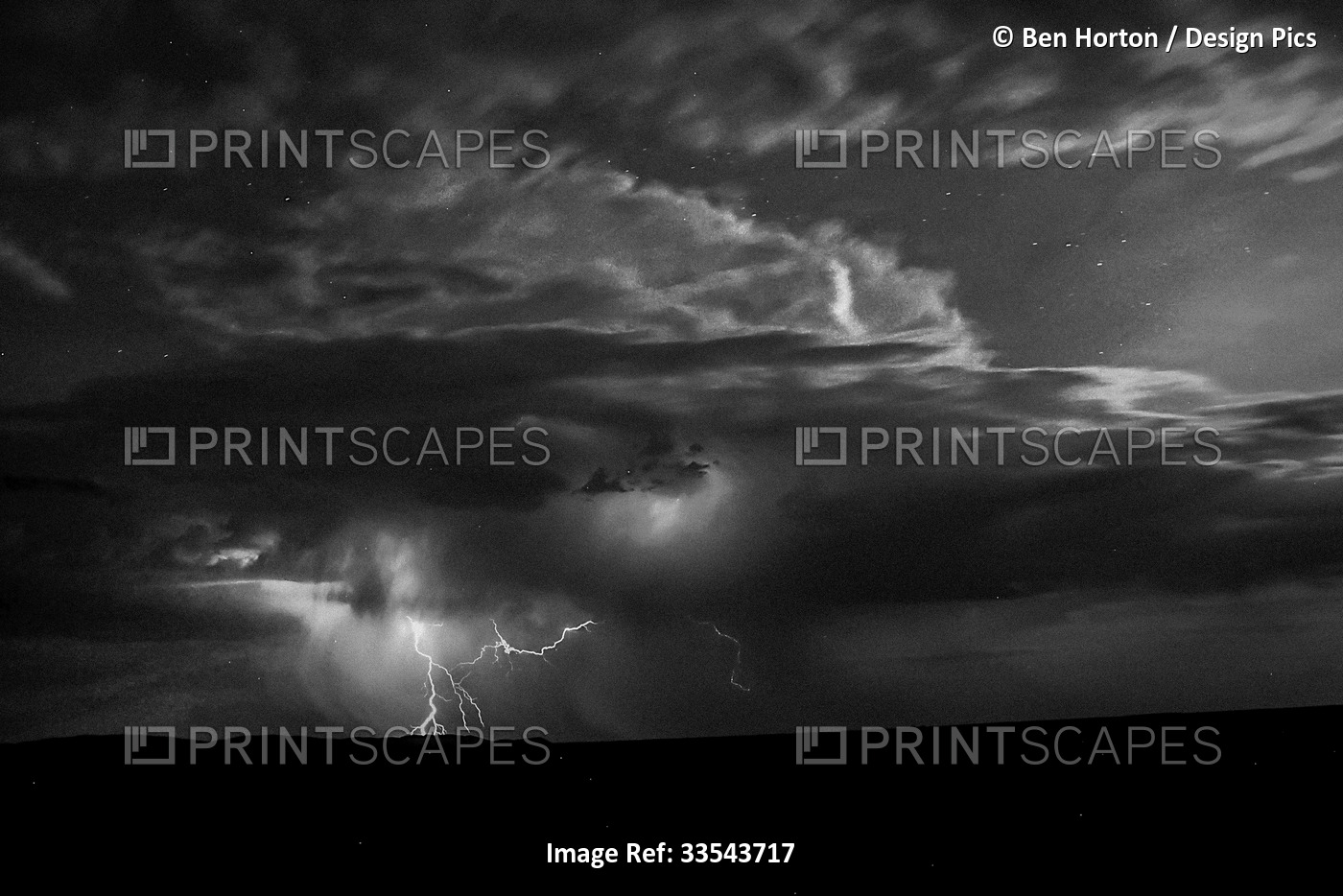 Lightning strikes from a night sky through storm clouds to the silhouetted ...