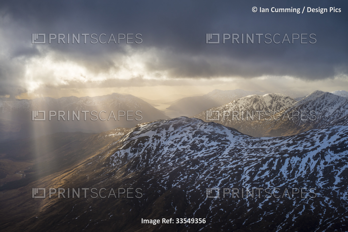 Sun breaking through cloud over snowy mountains near Glenfinnan; Scotland, ...