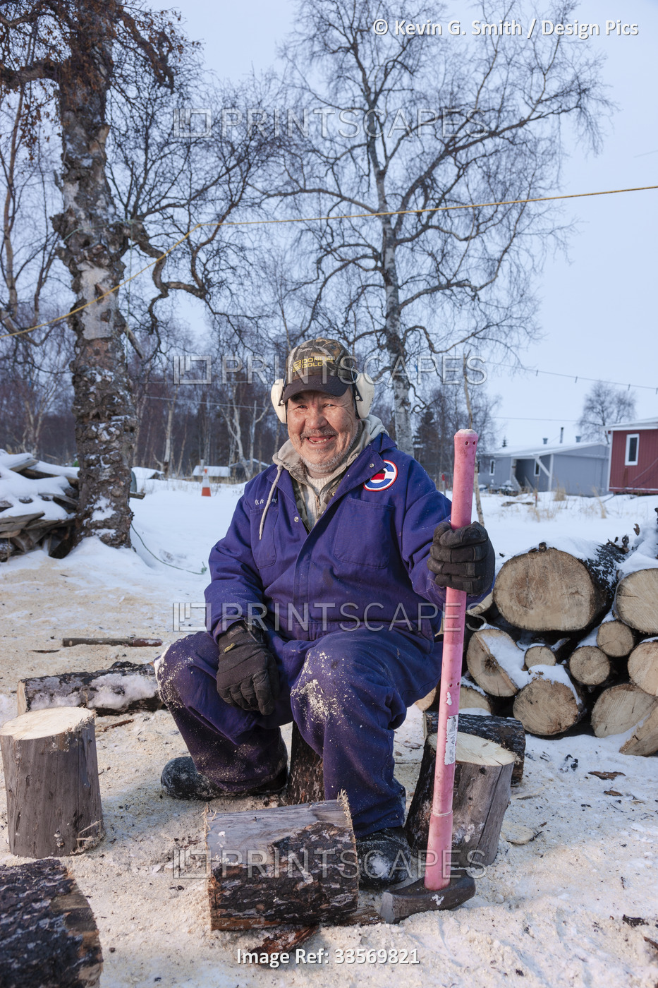 Male Alaska Native Yupiik Elder cutting wood for his wood stove with an axe in ...