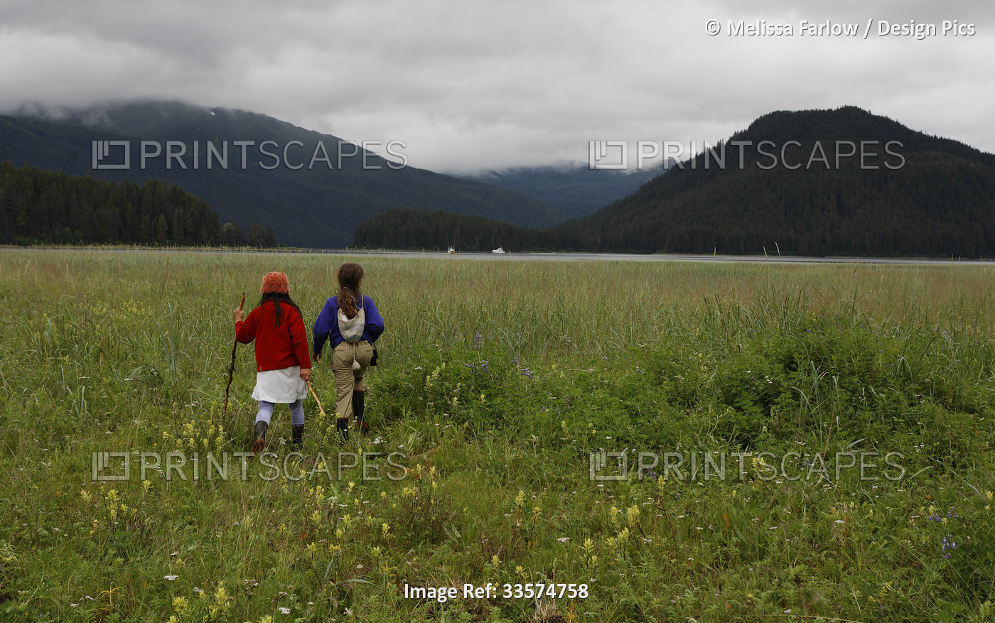View taken from behind of two young girls hiking through an uplift meadow with ...