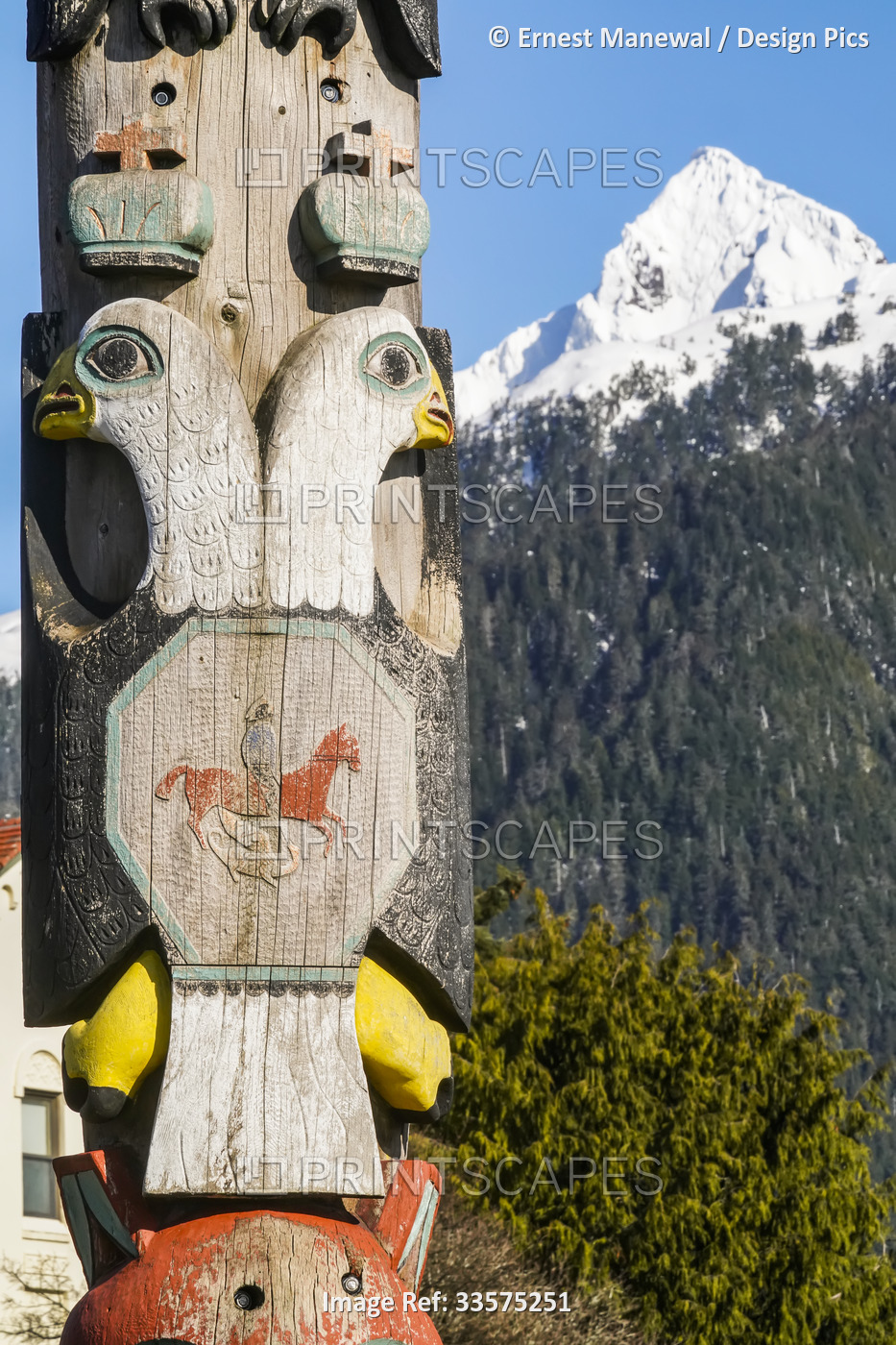 Close-up detail of a totem pole and the forested mountainside with snow-capped ...