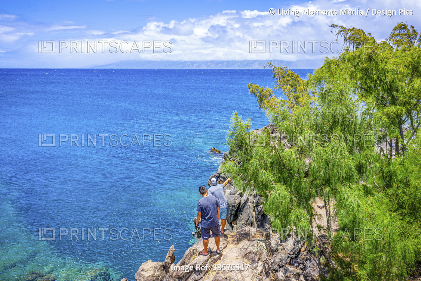 Two male tourists stand on the top of a rugged cliff looking out to the vast ...