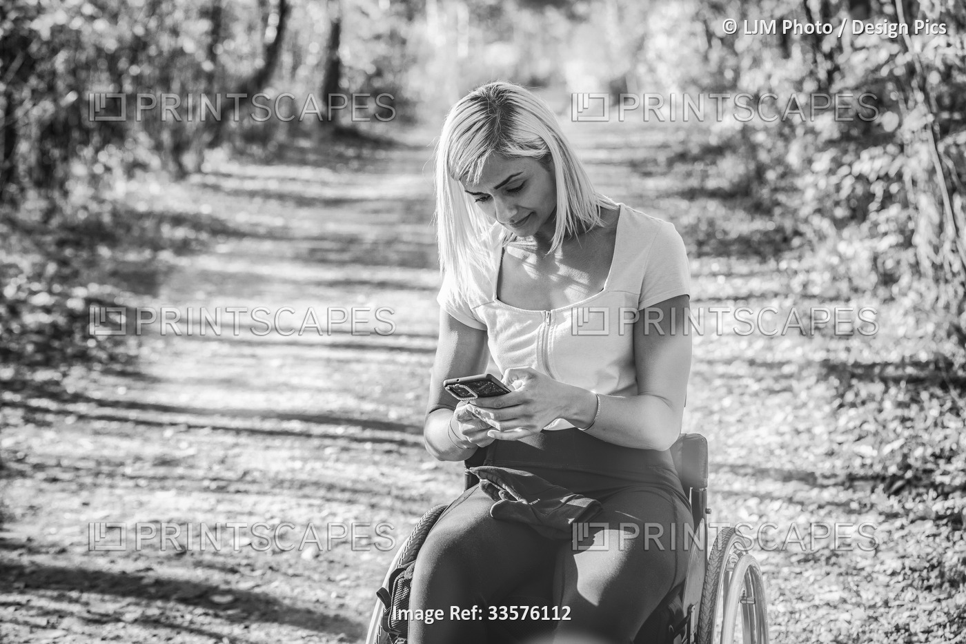 Young paraplegic woman in her wheelchair on a trail in a park using her smart ...