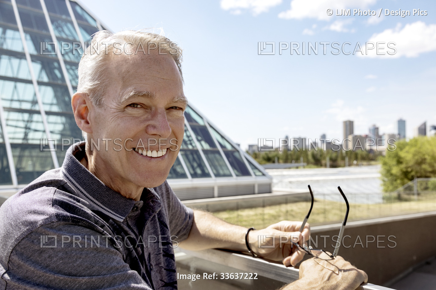 Outdoor portrait of senior man holding his eyeglasses, city skyline and modern ...
