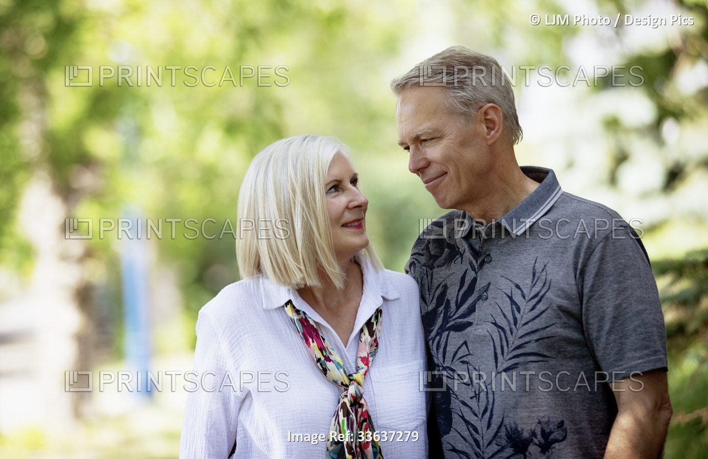 Outdoor portrait of a mature couple in a park as they stand and look at each ...