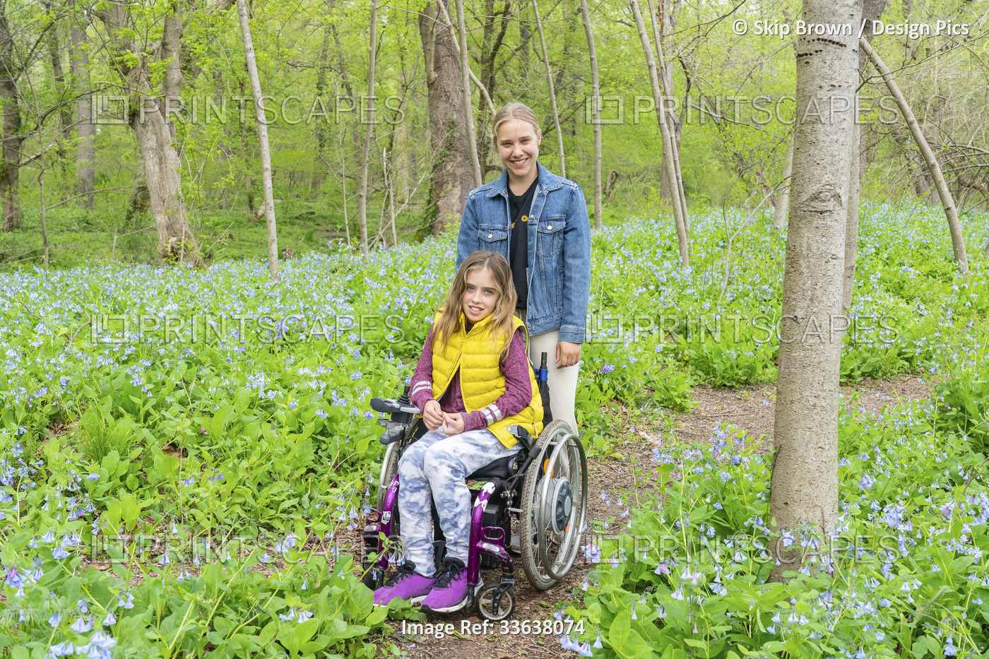 Girl in a wheelchair with her friend posing in the forest area while looking at ...