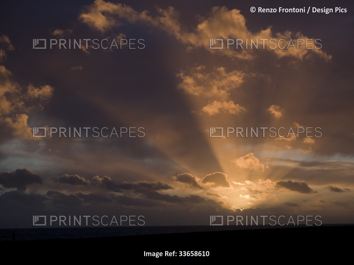 Sunset at sea with partly cloudy sky and sun rays; Brighton, East Sussex, ...