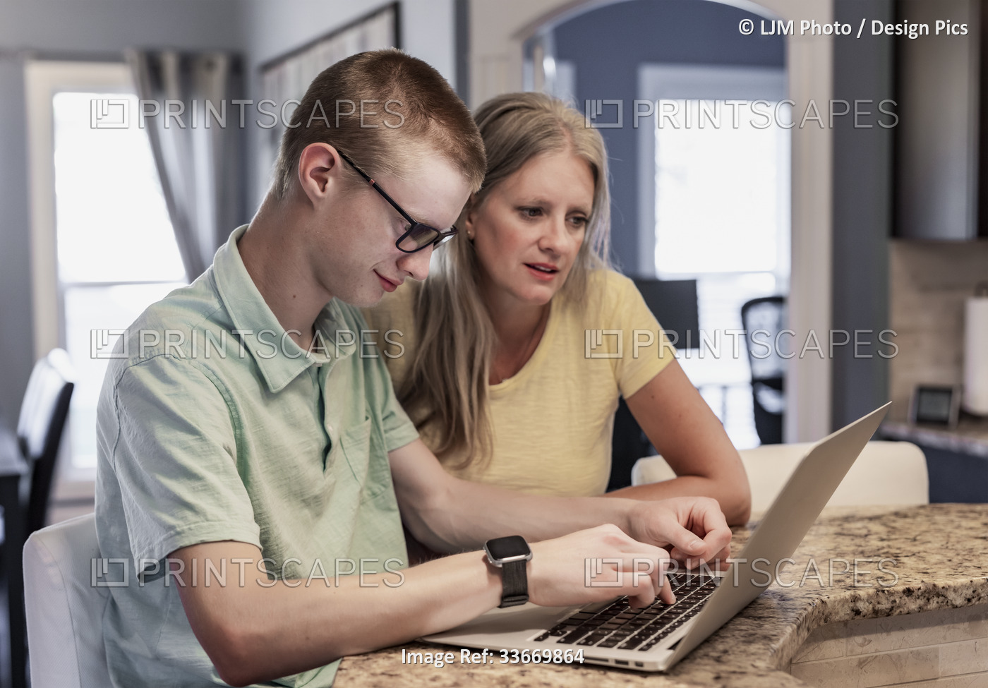 Young man uses a laptop computer at home with support from his mother; ...