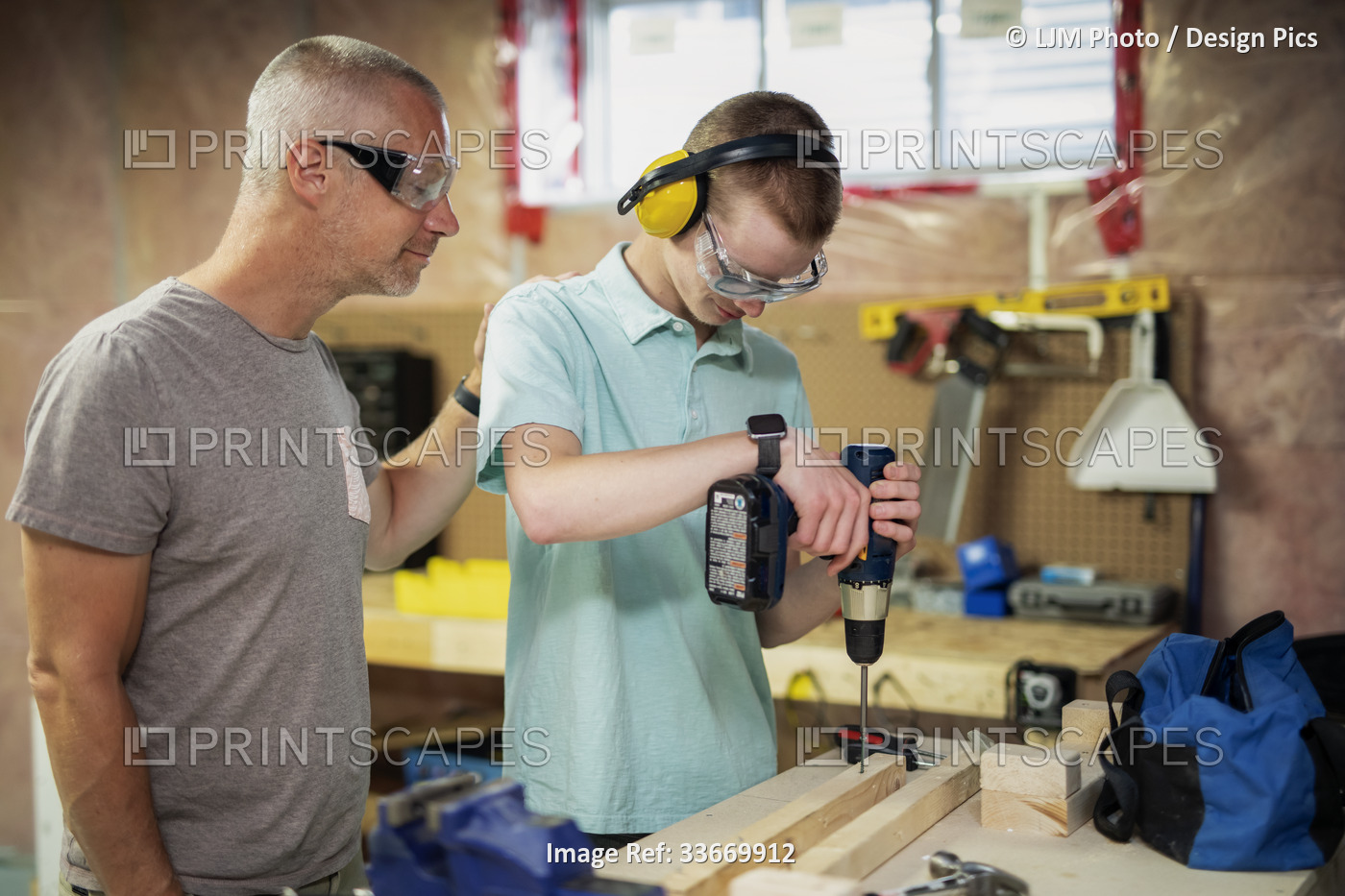 Young man doing woodworking in his basement while his father looks on; ...