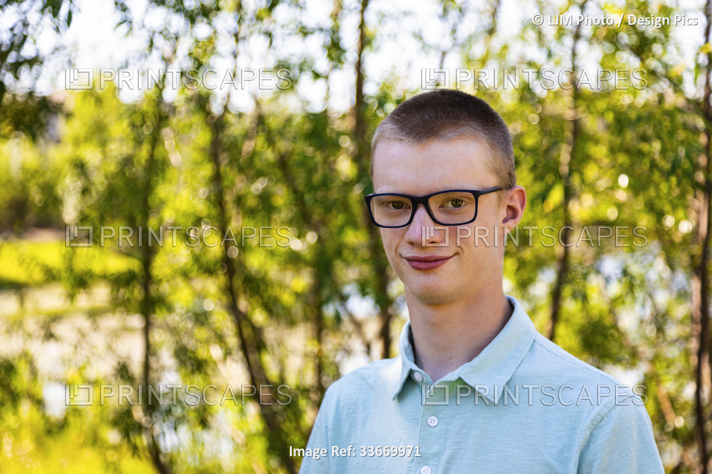Outdoor portrait of a young man with tree foliage and water in the background; ...