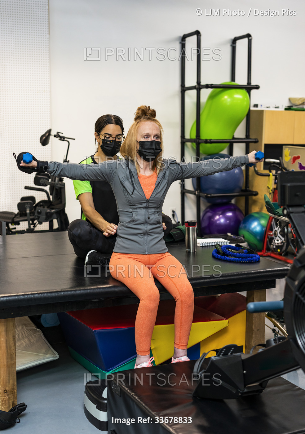 A paraplegic woman doing bilateral raises during her workout with her trainer: ...