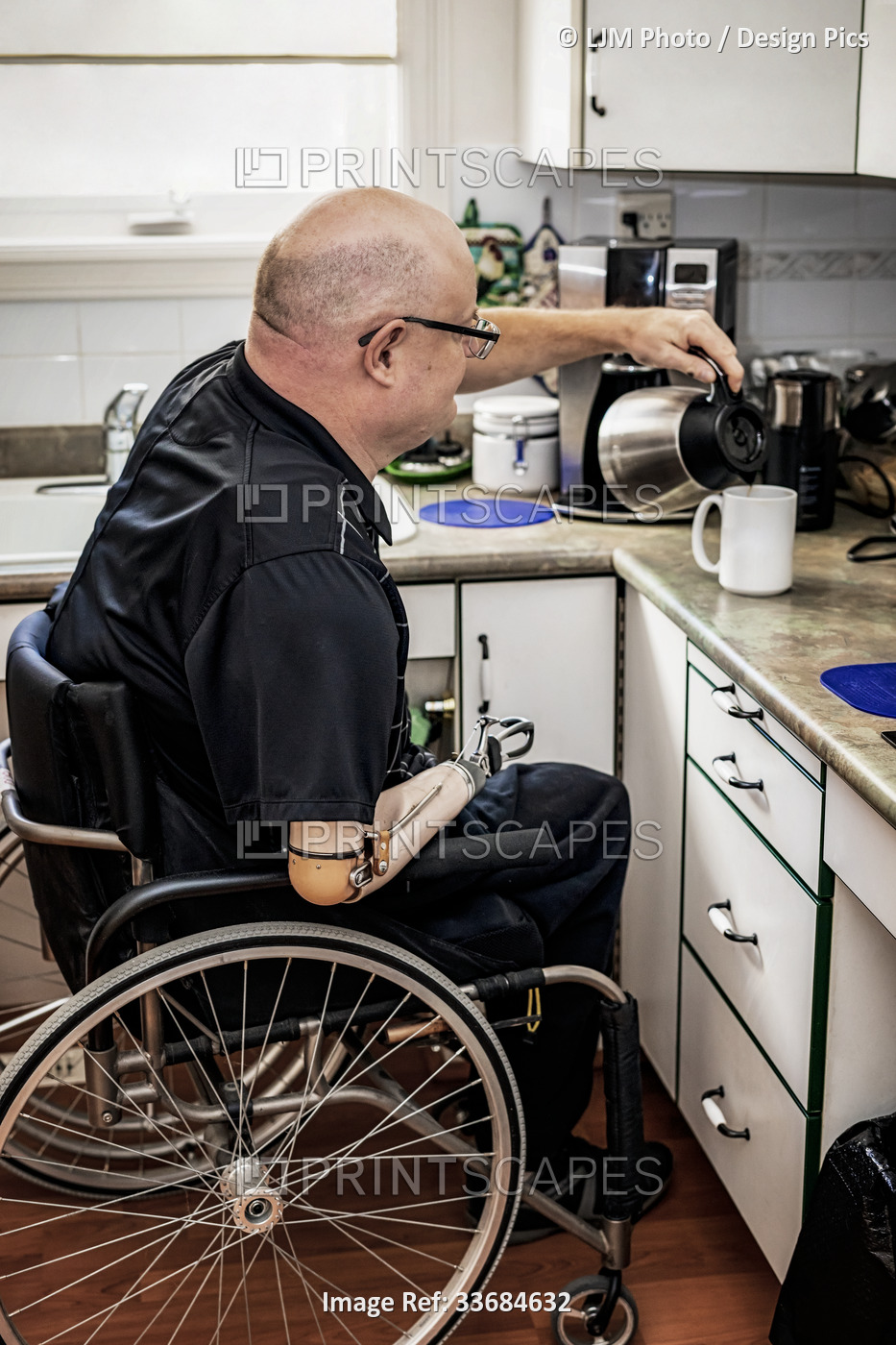 Man with double limb amputations pouring coffee in the kitchen at home; St. ...