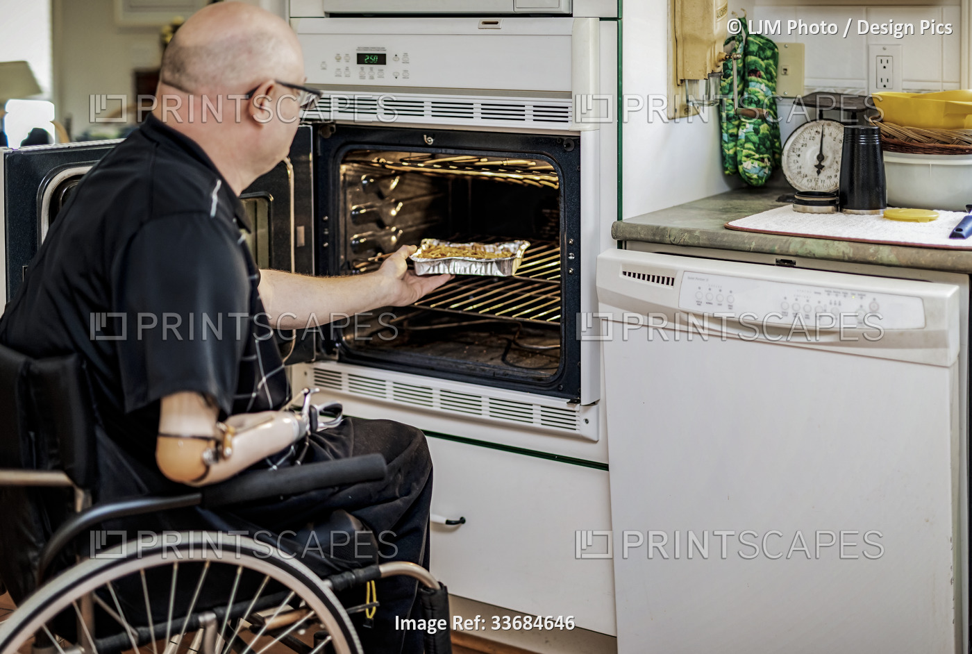 Man with double limb amputations using the oven in the kitchen at home; St. ...