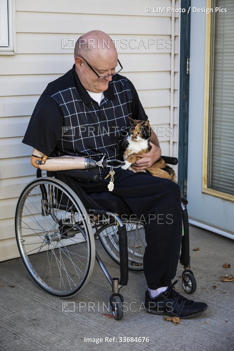 Man with double limb amputations sitting outside his house with his pet cat on ...