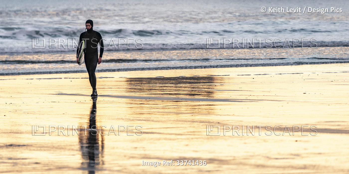 A surfer carries their surfboard on the wet sand at the popular surfing ...