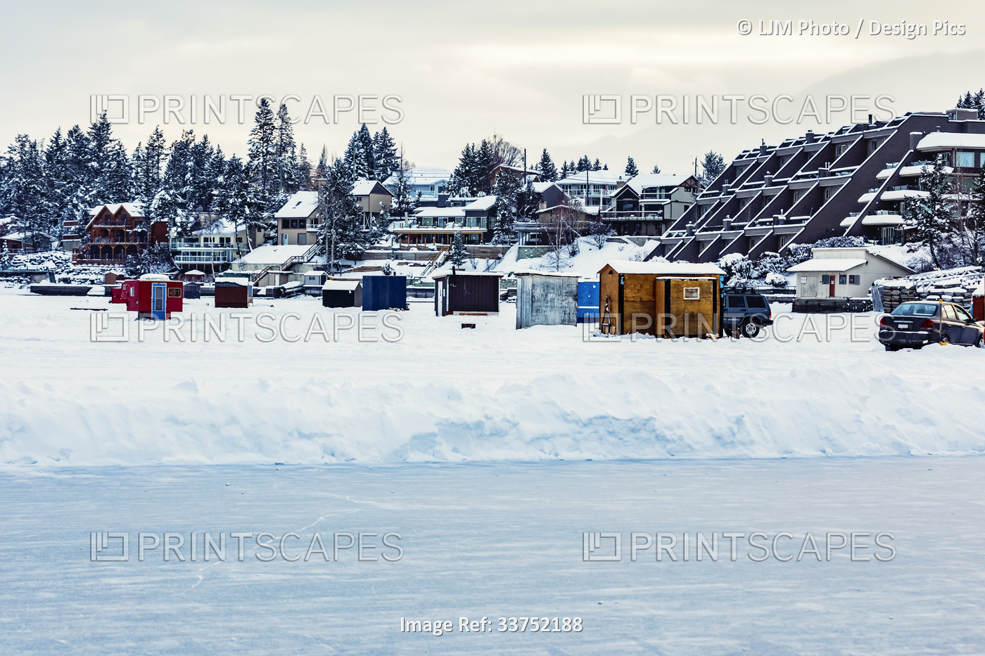 A view of a skating rink and ice fishing shacks and trailers on the shoreline ...
