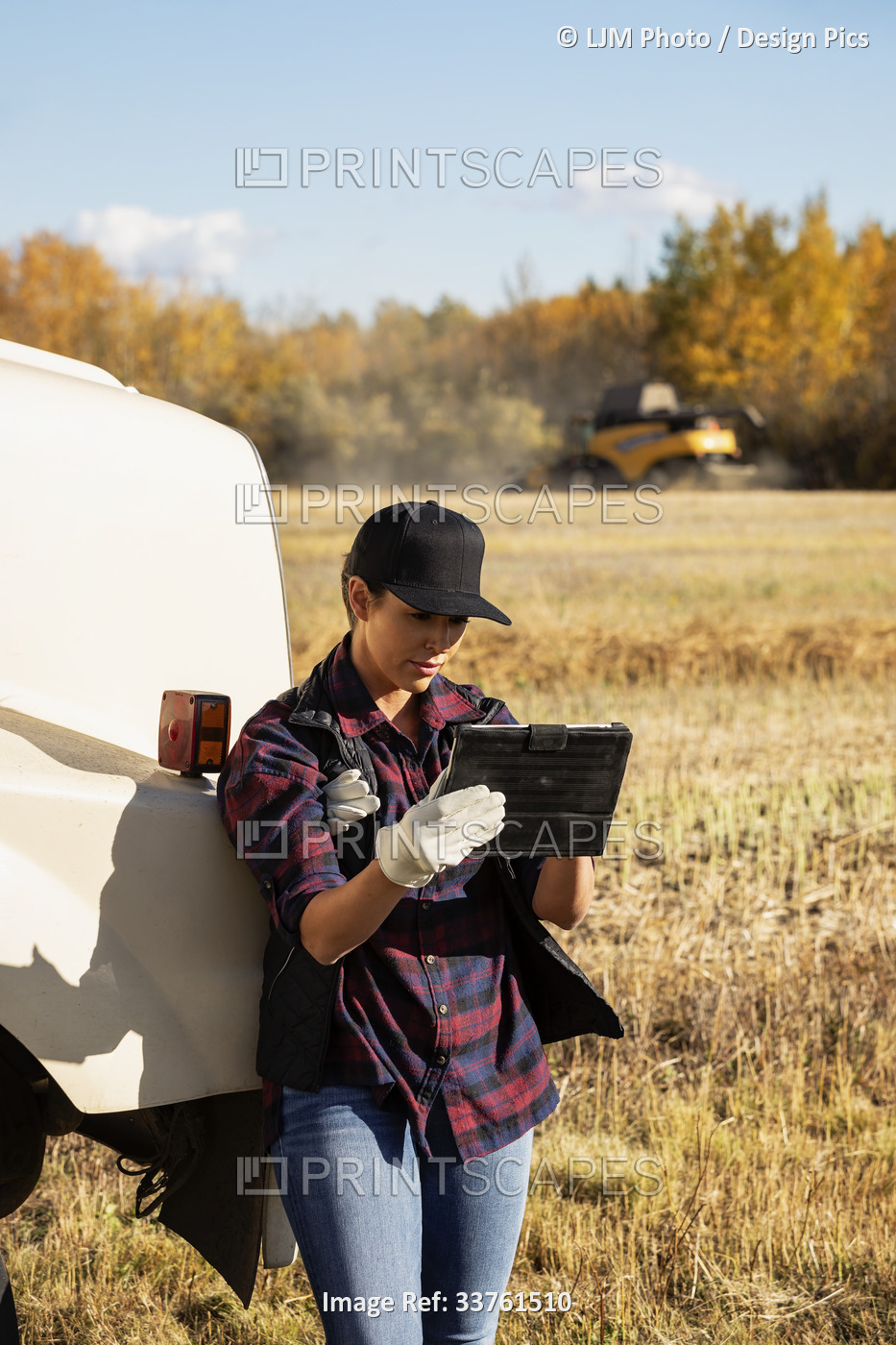 A woman standing beside a grain hauler and using a portable wireless device to ...