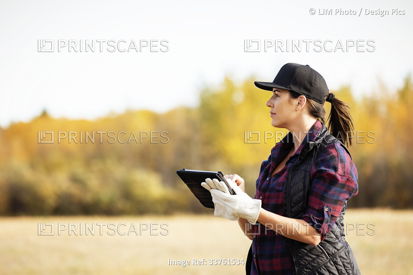 A woman standing in a field using a portable wireless device to manage and ...
