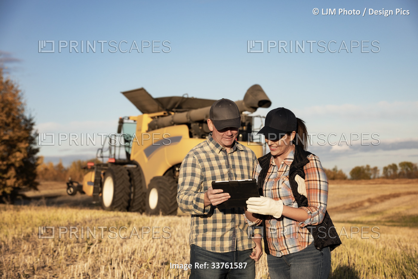 A husband and wife standing in front of a combine harvester and using a ...
