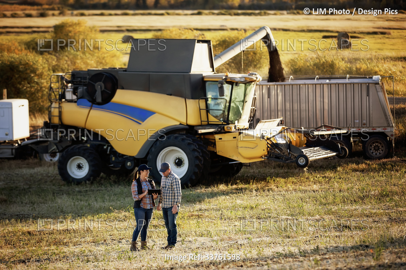 A farm couple standing in a field using a portable, wireless device to manage ...