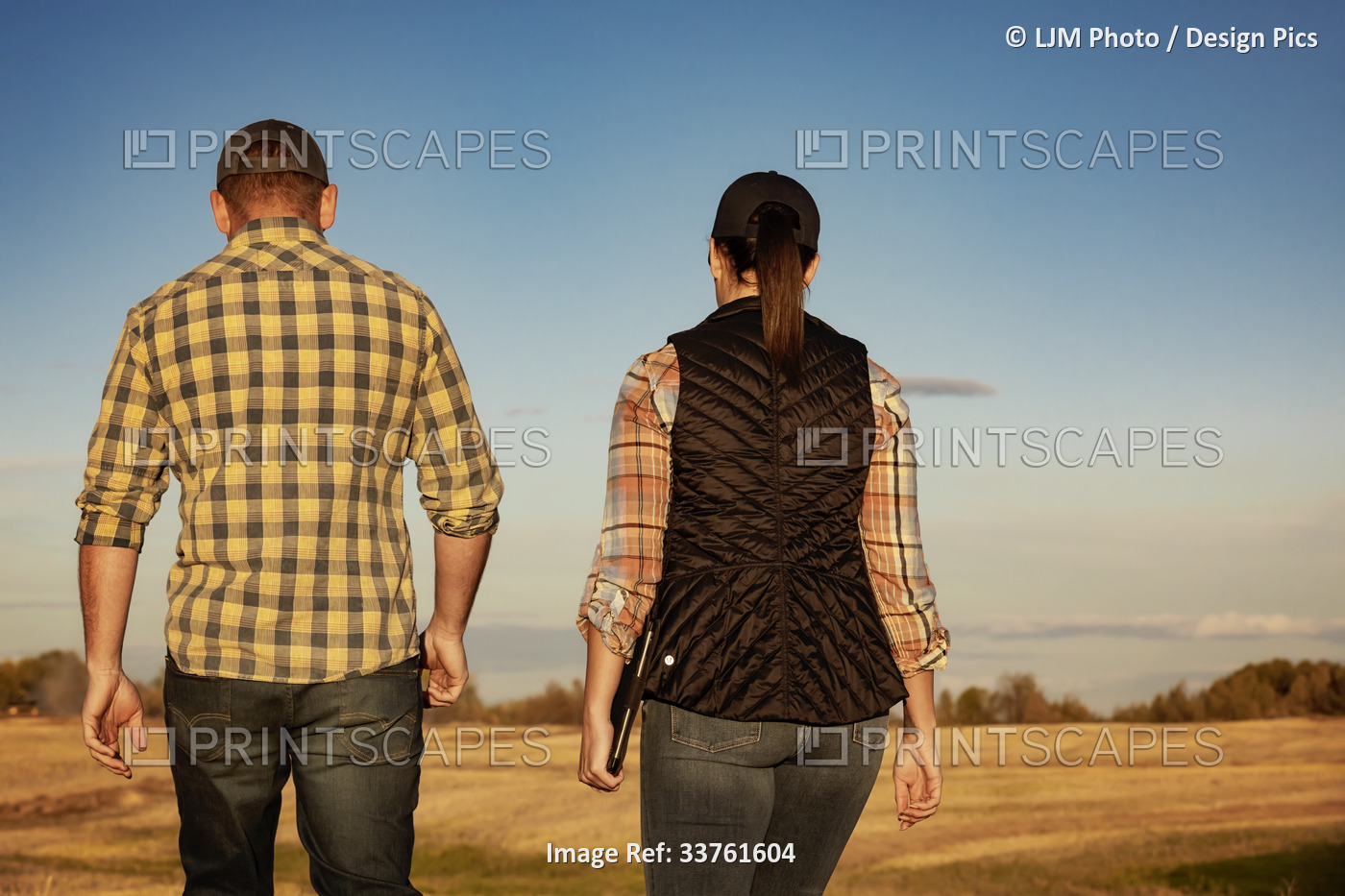 A view from behind of a husband and wife walking in a harvested field, spending ...