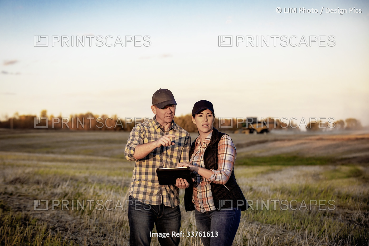 A husband and wife standing in the fields at twilight using a portable wireless ...