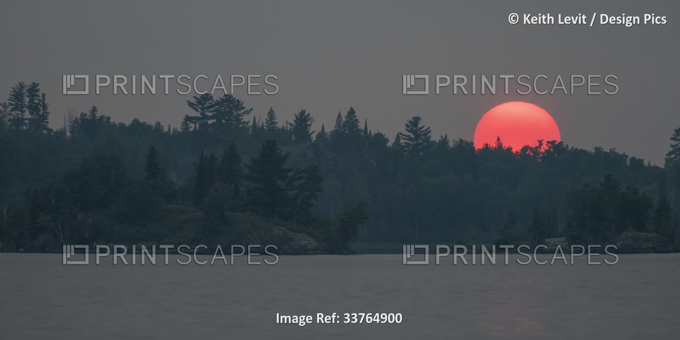 Vibrant pink sun glowing over silhouetted landscape and water at sunset, Lake ...