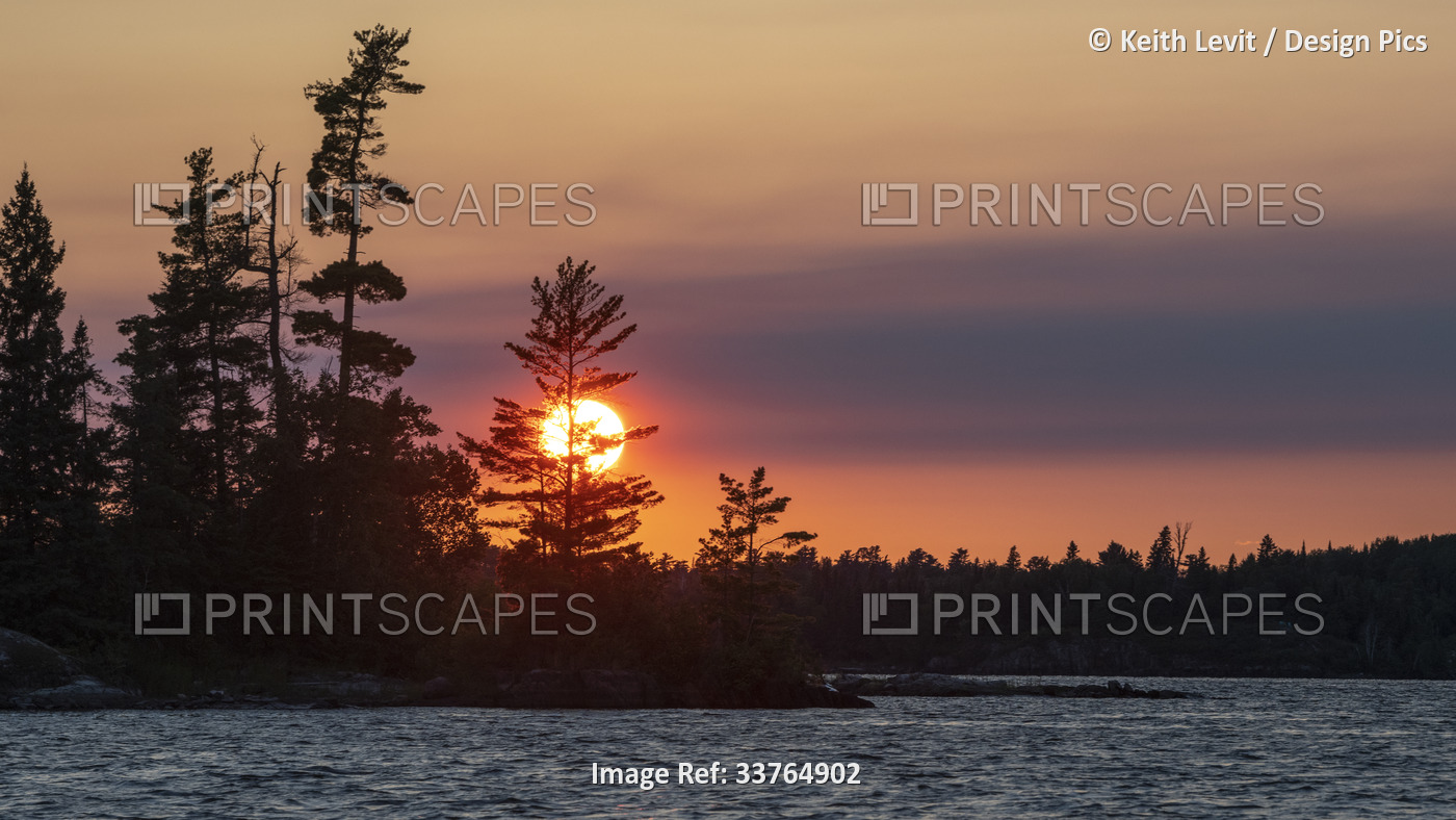 Vibrant sun glowing over silhouetted landscape and water at sunset, Lake of the ...