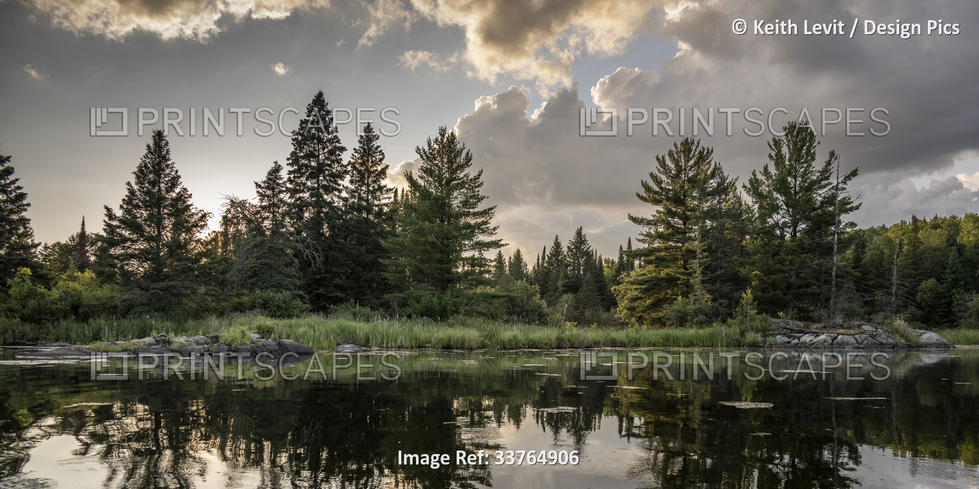 Sunset light warms a scenic landscape and it's mirror image is reflected on ...