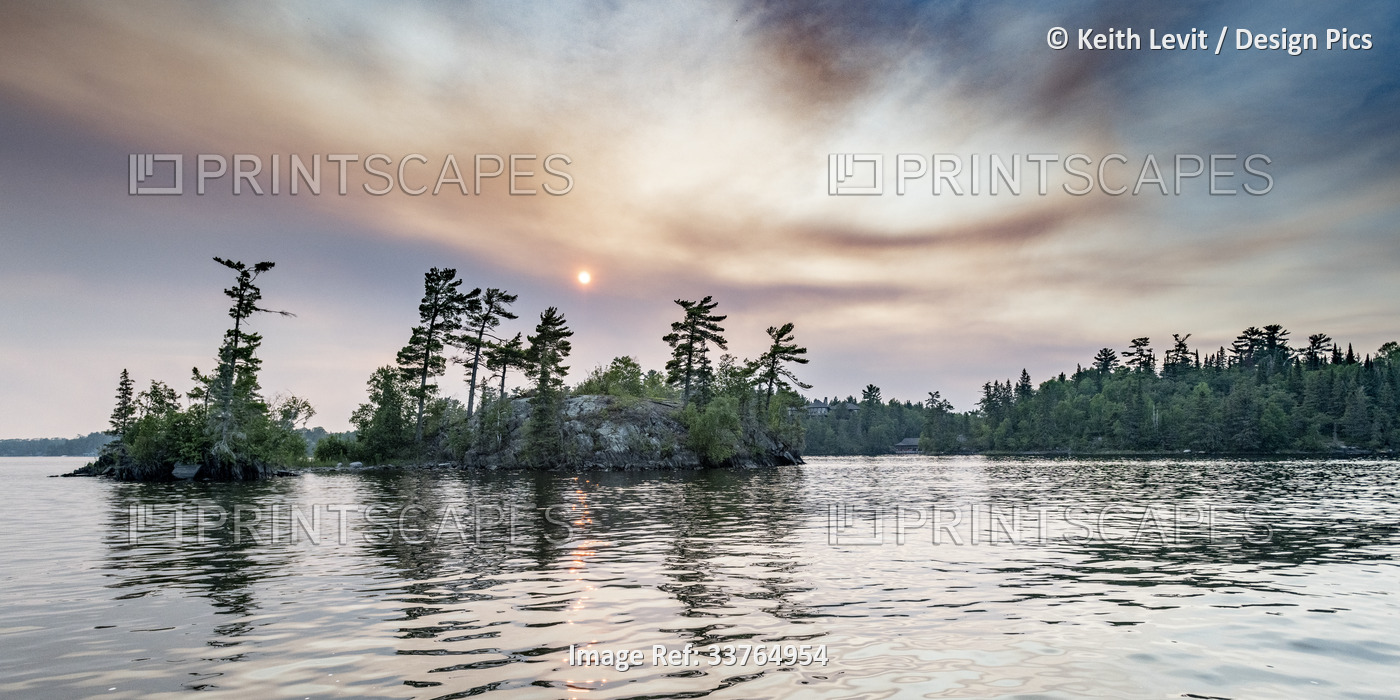 Sun glowing in clouds over a lake and forest at sunset, Lake of the Woods, ...