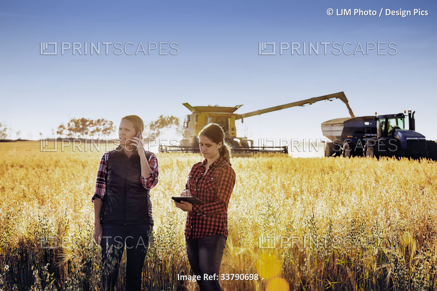 A mature farm woman standing in a field making a call while a younger woman ...