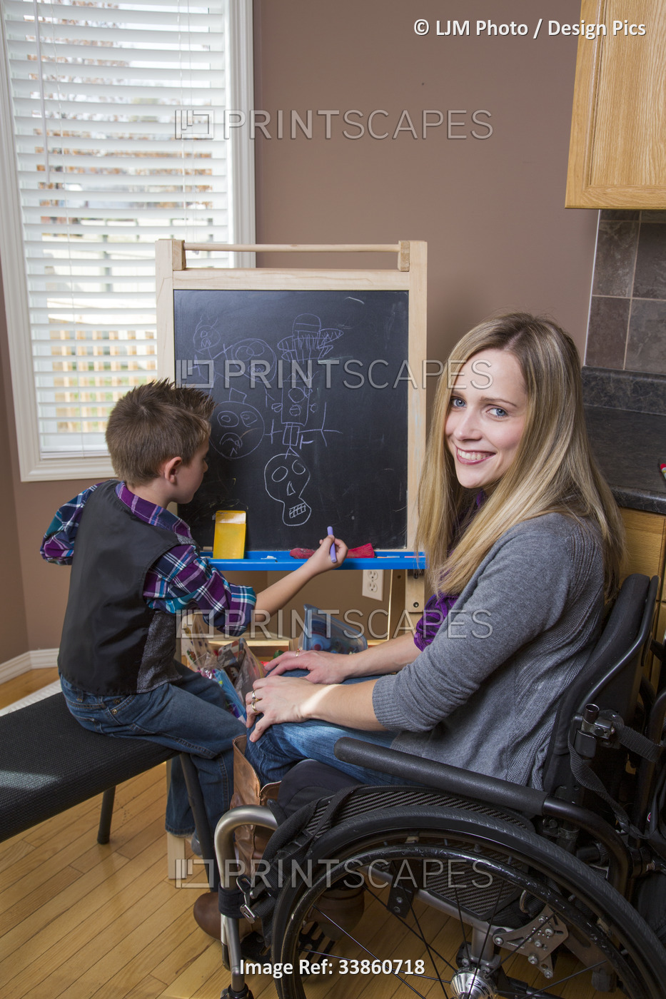 Young paraplegic mother teaching her son and drawing on a chalkboard together ...