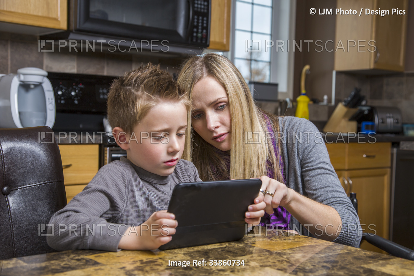 Disabled mother helping her son learn on a tablet at home; Spruce Grove, ...