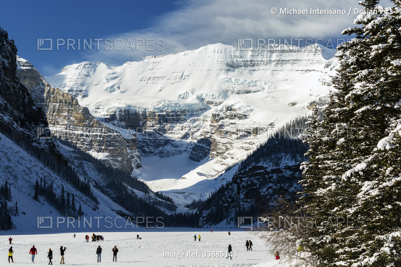 Several people on frozen Lake Louise overlooking a snow-covered mountain with ...