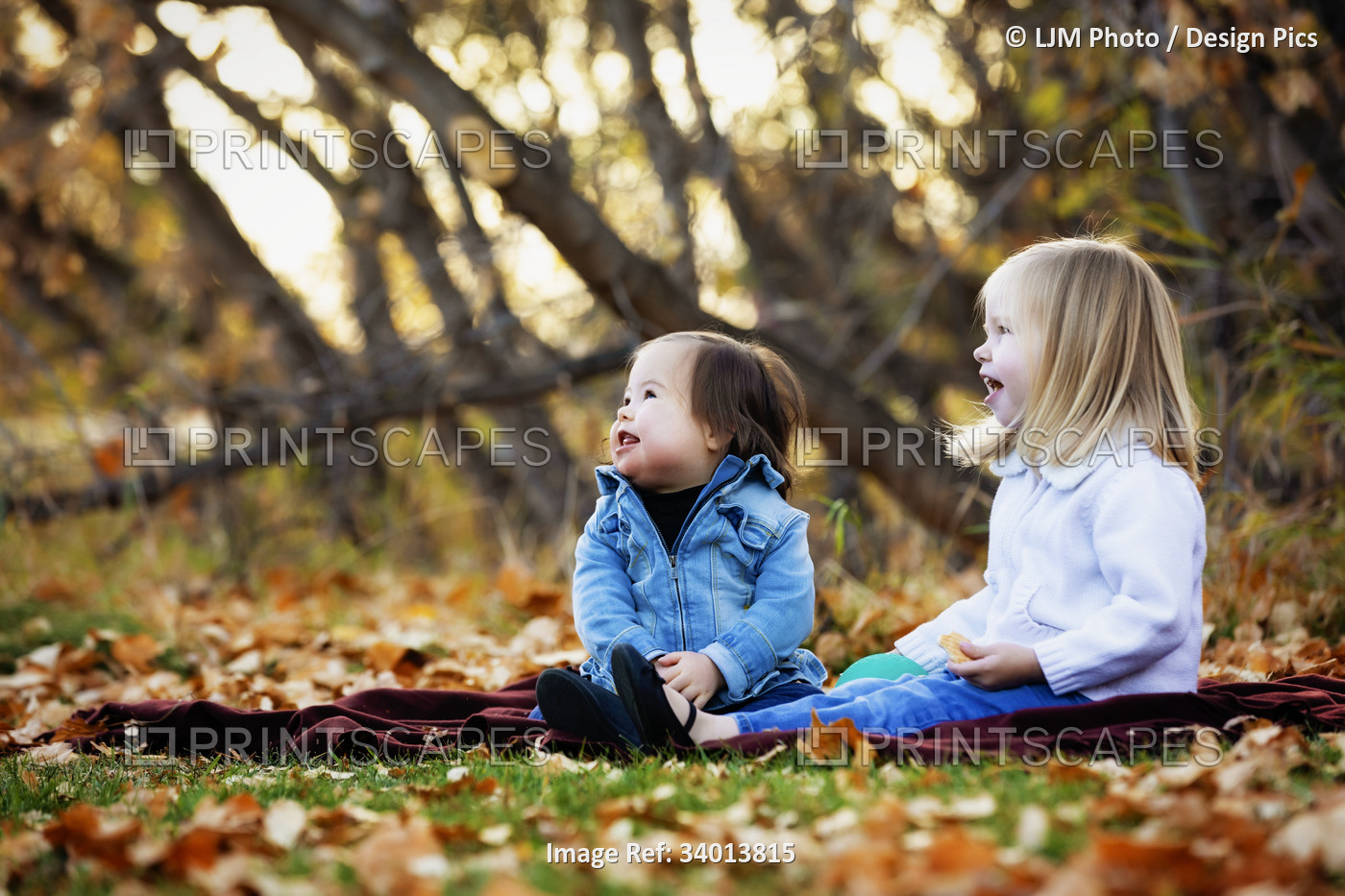 Two young sisters, one with Down Syndrome, playing together in a city park ...
