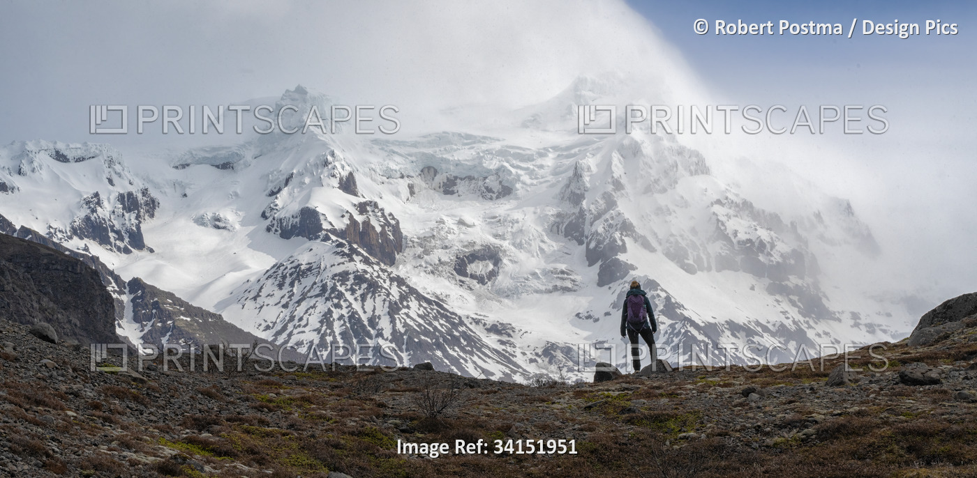 Woman standing in the drizzle in front of an imposing mountain with a glacier ...