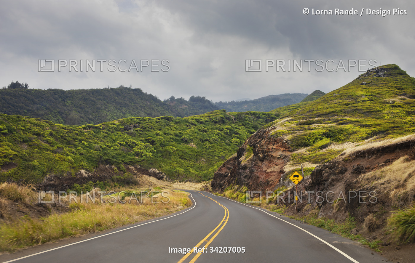 Winding road with traffic sign and cloudy sky through the green hills along a ...