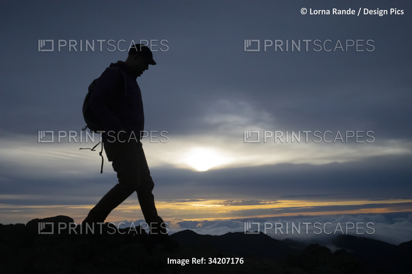 Silhouette of man wearing a backpack, walking on volcanic rocks on a mountain ...