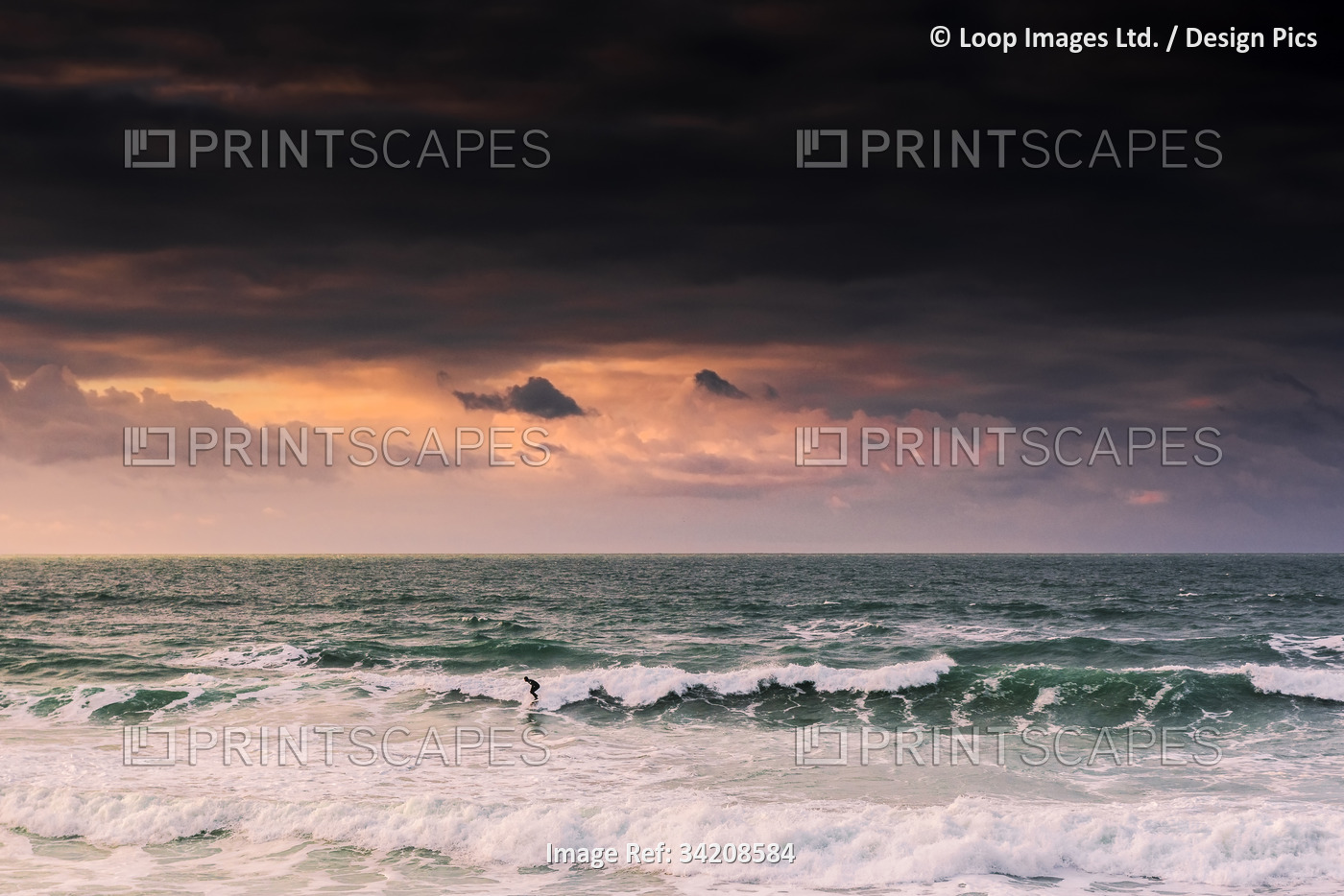 A spectacular sunset as a lone surfer rides a wave at Fistral Beach in Newquay ...