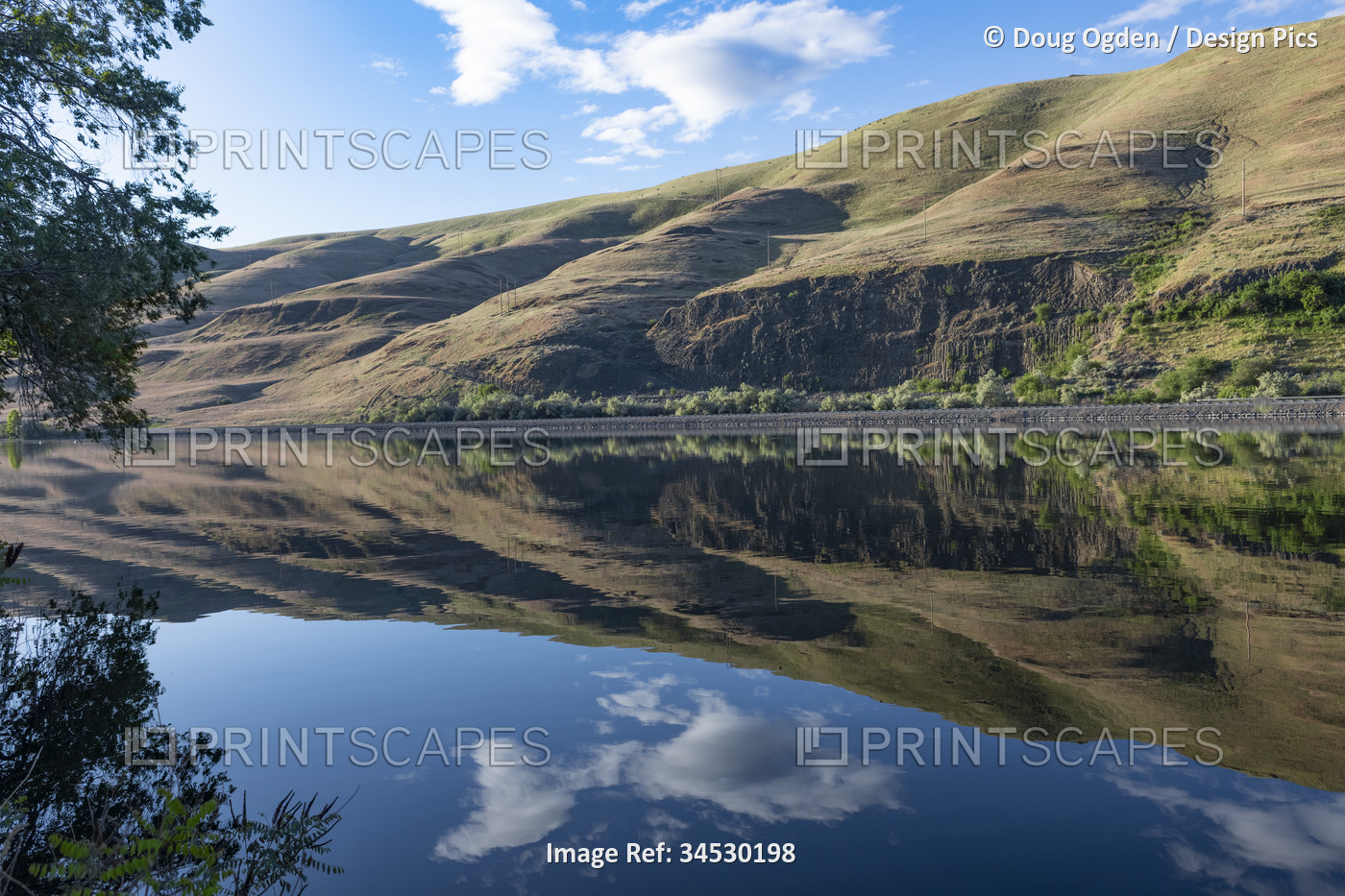 Reflection of the rolling hills and blue sky on a perfectly calm Snake River ...