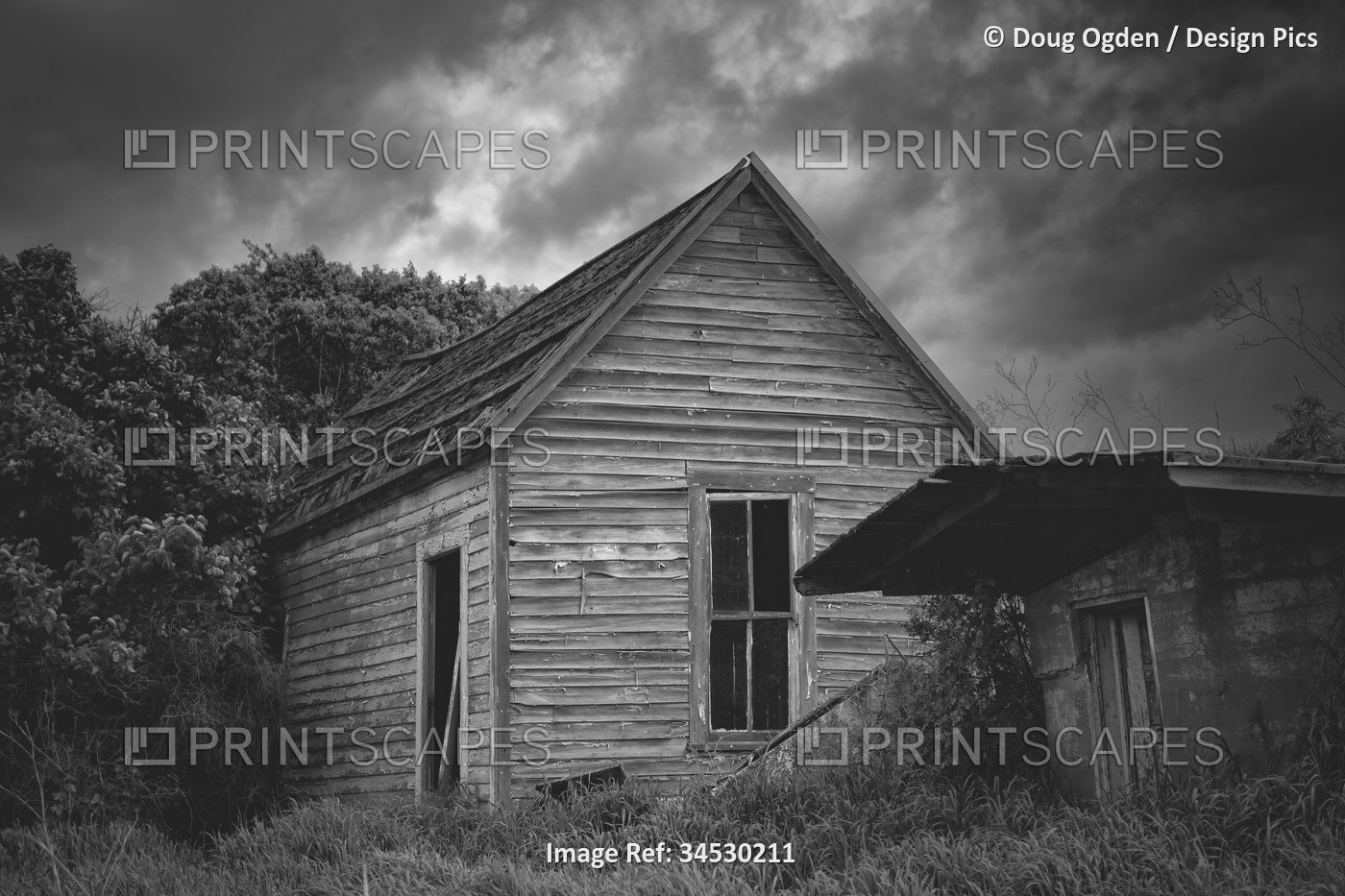 Black and white image of a spooky old abandoned house under threatening weather ...