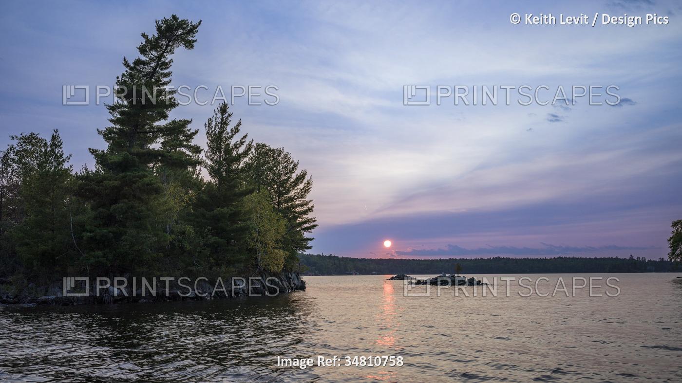 Picturesque sunset over a lake with a pink sunbeam reflected on the tranquil ...