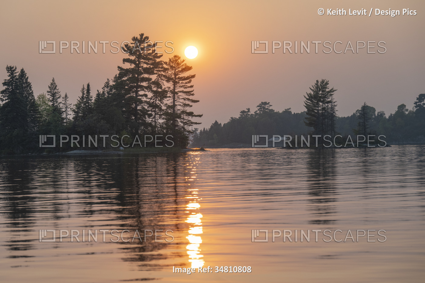 Dramatic sunset light over a lake with silhouetted trees along the shoreline ...