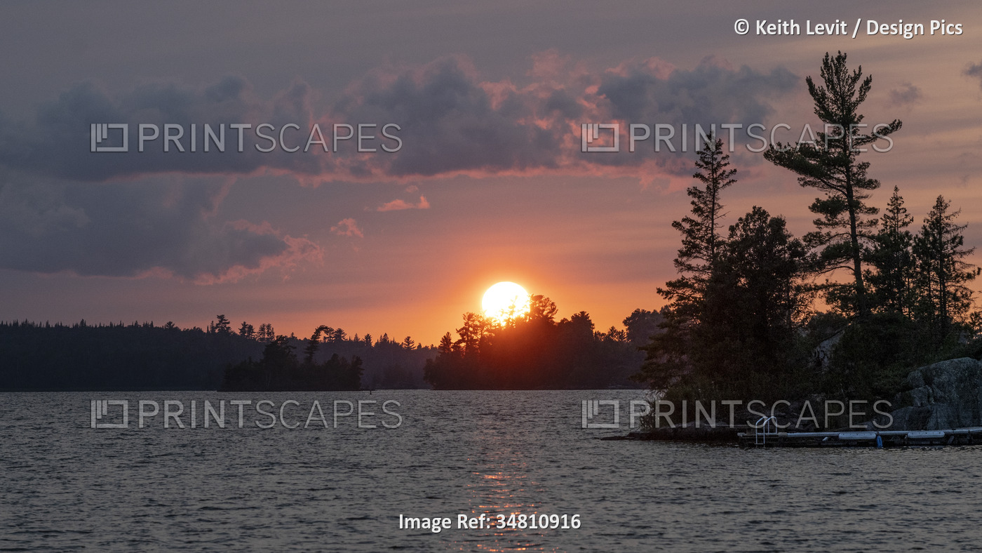 Dramatic view of the warm glowing sun sinking over the horizon with a lake and ...